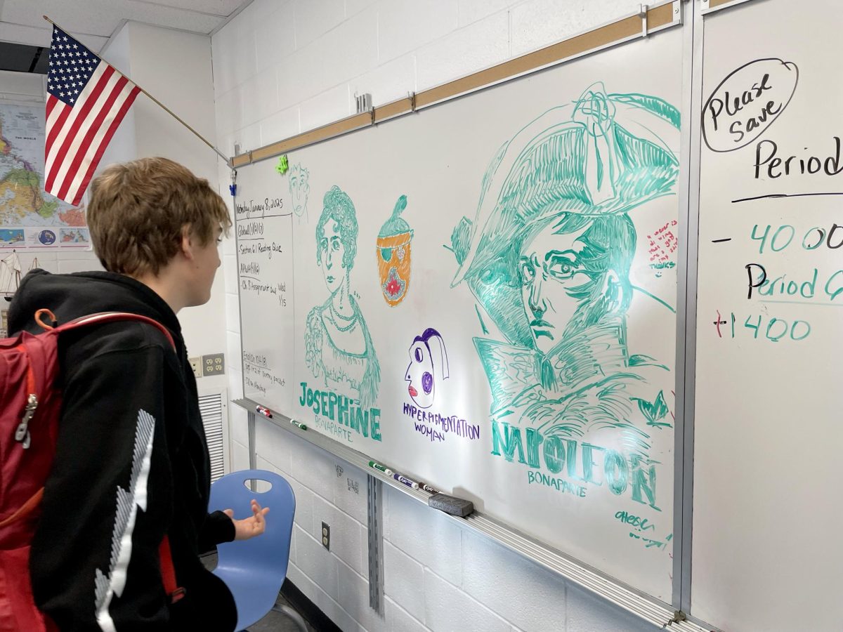 Henry Foley-Hedlund admires portraits of Josephine and Napoleon Bonaparte created by sophomores Dessa Bellamy Tarantino and Alexa Arcigal, respectively, on Michelle Cordaro's whiteboard during AP World History Class.